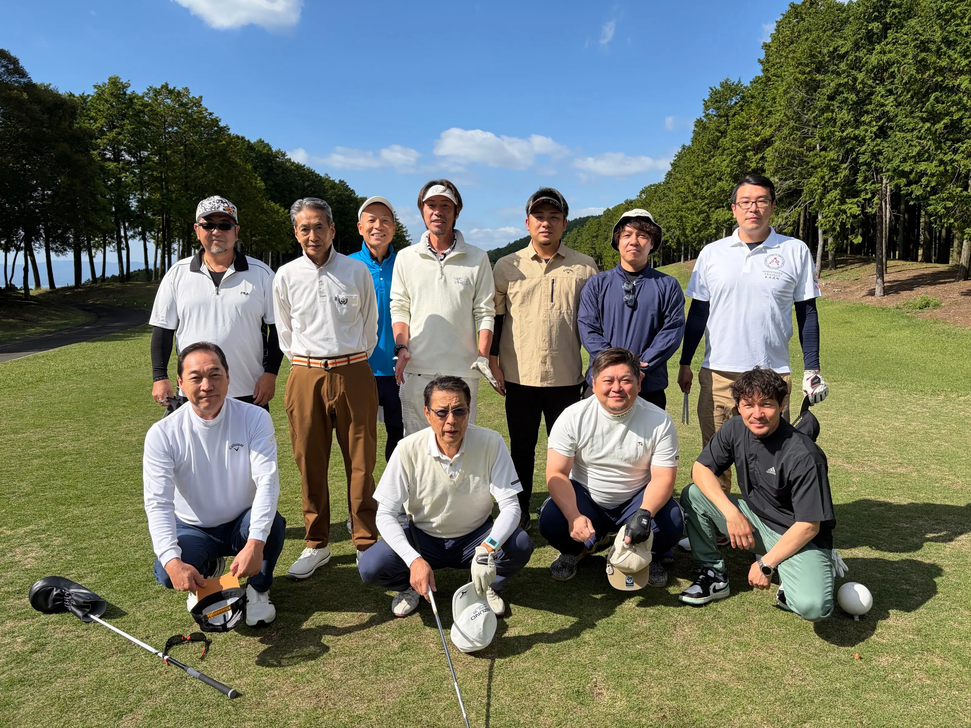 ゴルフコンペに参加した本石灰町自治会の皆さんの集合写真。青空の下、コースの芝の上で